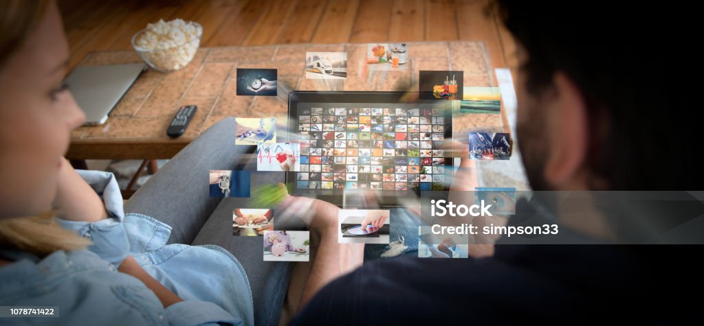 Couple using tablet for watching VOD service Couple using tablet for watching VOD service. Video On Demand television with abstract flying images Downloading Stock Photo