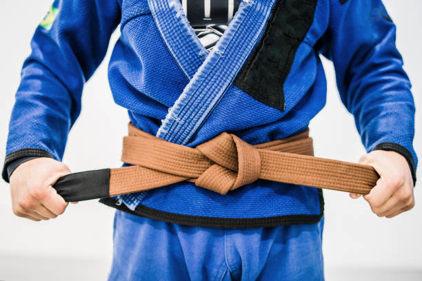 Close up of a bjj brown belt Midsection of Brazilian jiu jitsu Fighter in a gi Holding a bjj brown belt tied around his waist. brazilian jiu jitsu photos stock pictures, royalty-free photos & images