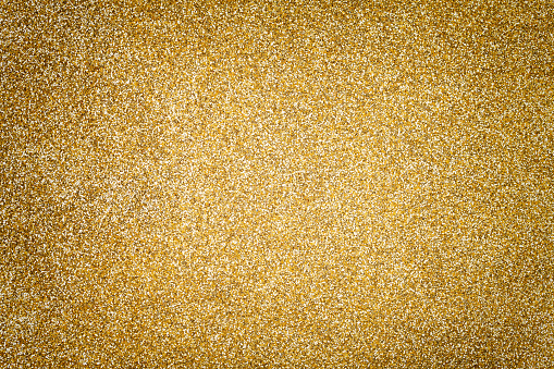 Golden sparkling background from small sequins, closeup. Brilliant shiny backdrop from textile. Shimmer yellow paper with vignette
