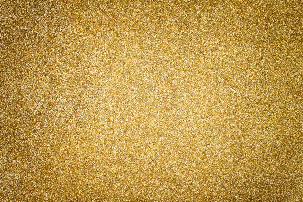 Golden sparkling background from small sequins, closeup. Brilliant shiny backdrop from textile. Shimmer yellow paper with vignette