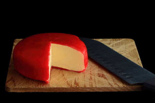 Gouda Cheese Wheel of Gouda Cheese covered with red wax protective layer over wooden cutting board, knife with which is cut a segment (wedge) of the cheese in order cheese to be seen over black background gouda cheese stock pictures, royalty-free photos & images