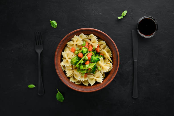 istock Farfalle pasta with vegetables on the plate. Top view. On a black background. Free copy space. 1078907066