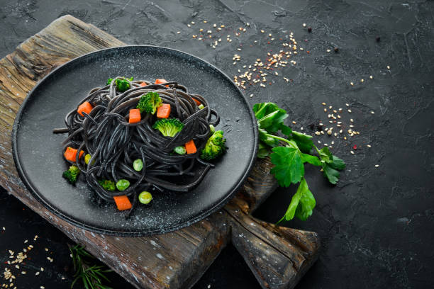 istock Black pasta with vegetables on a black plate. Top view. On a black background. Free copy space. 1078915322