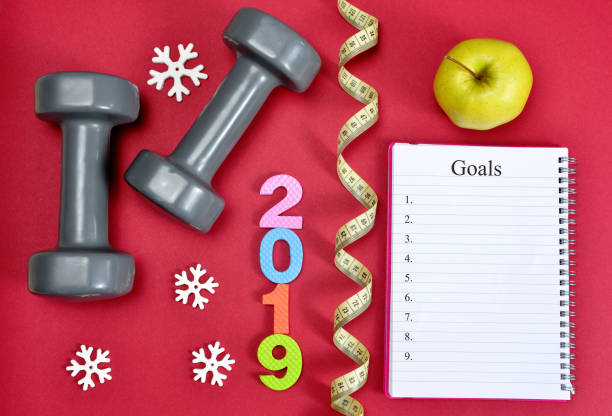 Healthy resolutions for the New Year 2019. Dumbbells with apple and open notebook on red background. Healthy resolutions for the New Year 2019. 2019 new year resolution stock pictures, royalty-free photos & images