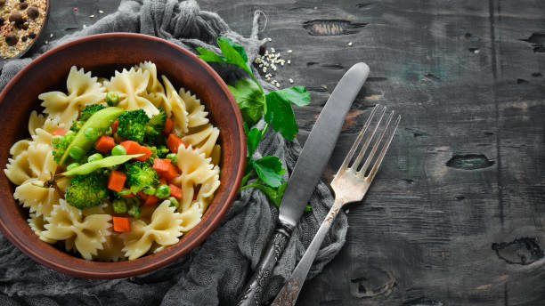 istock Farfalle pasta with vegetables on the plate. Top view. On a black background. Free copy space. 1078949270