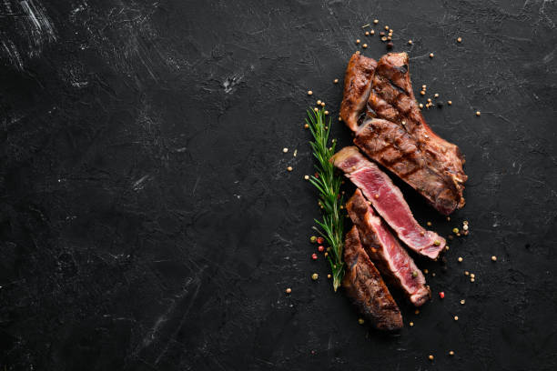 istock Veal steak on a bone on a black background. Free space for your text. Top view. 1078972316