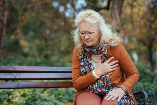 elderly woman having chest pains or heart attack in the park - chest pain imagens e fotografias de stock