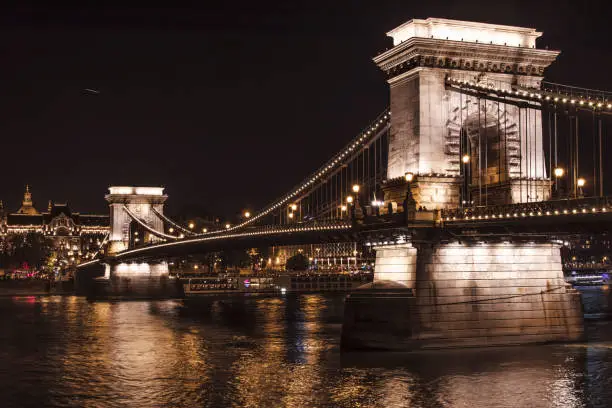 Bridge through the Danube river at night with view at the houses in Budapest with bright night colors of the Hungarian Capital.