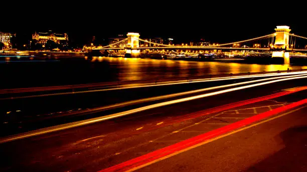 Red lines from the cars on the Danube river at night with view at the main bridge in Budapest with bright night colors of the Hungarian Capital.