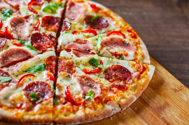 モッツアレラ チーズ、ハム、トマトソース、サラミ、唐辛子、スパイス、新鮮なルッコラのピッツァ。木製のテーブル背景にイタリアのピザ - pepper ストックフォトと画像