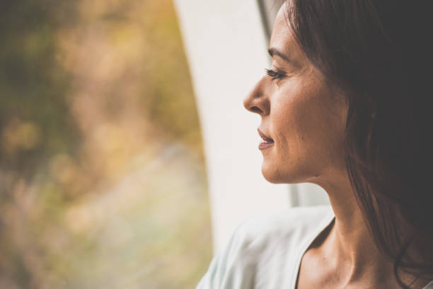 istock Pensive woman looking through window 1079028890