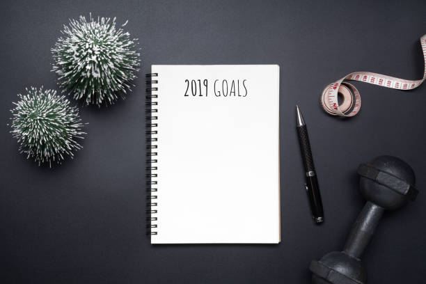 istock 2019 new years resolutions sport flat lay composition. Black dumbbells, measuring tape, blank notebook and mini Christmas tree on black background. New year new healthy and dieting goals concept. Top view with copy space. 1079037062