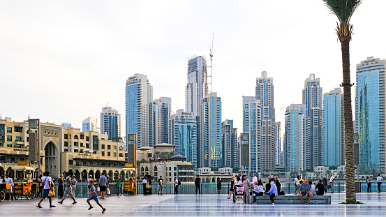 Dubai, United Arab Emirates  - October 31, 2018: Tourists and locals at the Dubai Mall square in the downtown district, with urban skyline in the background.