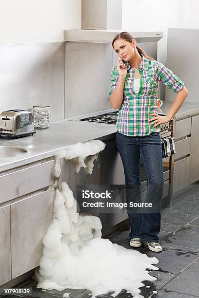 Young Woman On Phone With Overflowing Dishwasher — стоковые фотографии и другие картинки Посудомоечная машина - Посудомоечная машина, Переливающийся, Кухня