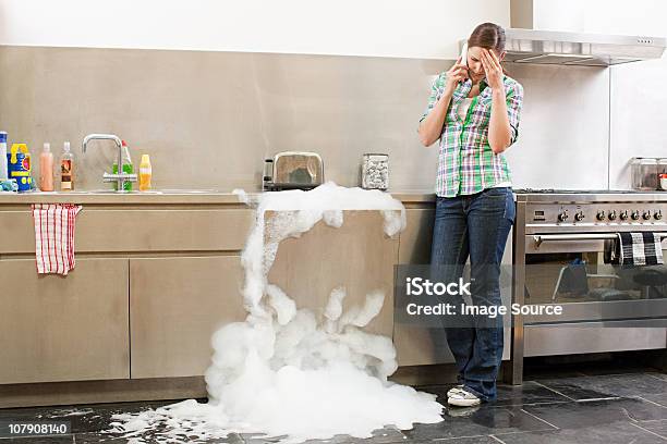 Young Woman On Phone With Overflowing Dishwasher Stock Photo - Download Image Now - Dishwasher, Overflowing, Messy