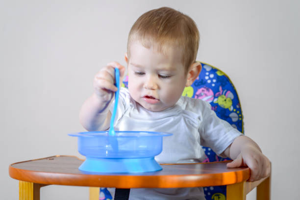 istock Little baby boy learning to eat at a table studying a plate and spoon in the kitchen 1079082166