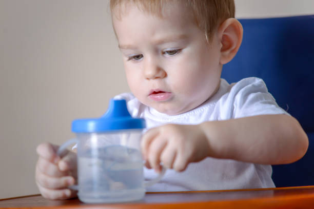 istock Baby boy drinking water studying a plastic bottle while sitting on a chair in the kitchen. 1079082230