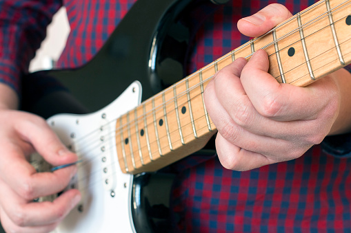Hands of a man in a plaid shirt playing black guitar