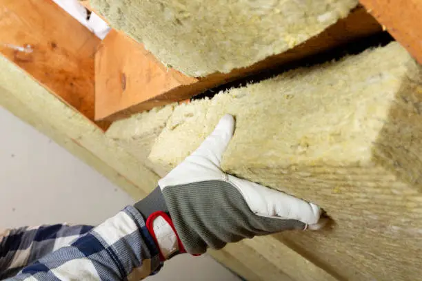 Man installing thermal roof insulation layer - using mineral wool panels. Attic renovation and insulation concept
