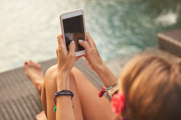 istock Girl using cellphone while lying on a swimming pool deck lounge bed. 1079093946