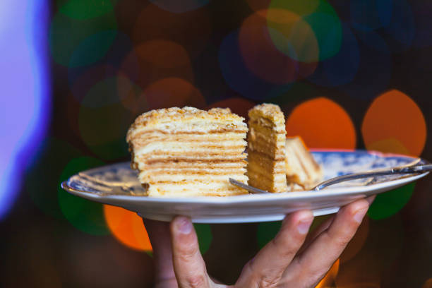 Appetizing piece of cake lies on a plate close-up. In the background blurred bright lights of Christmas garland.