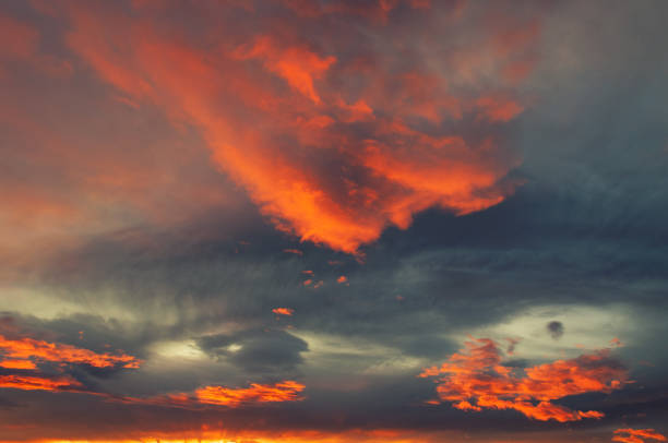 Dramatic radiant fiery orange clouds lit by setting sun in foreground and gray clouds in background
