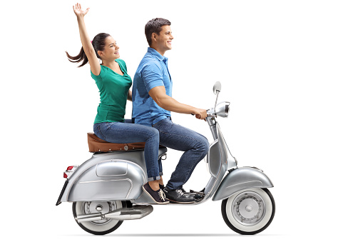 Full length profile shot of a young couple riding on a vintage motorbike and waving isolated on white background