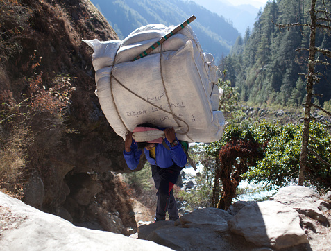 Namche Bazaar, Khumbu, Nepal - January 17, 2017: Nepalese porter carrying a heavy load to the pass in Sagarmatha National Park, Himalayas