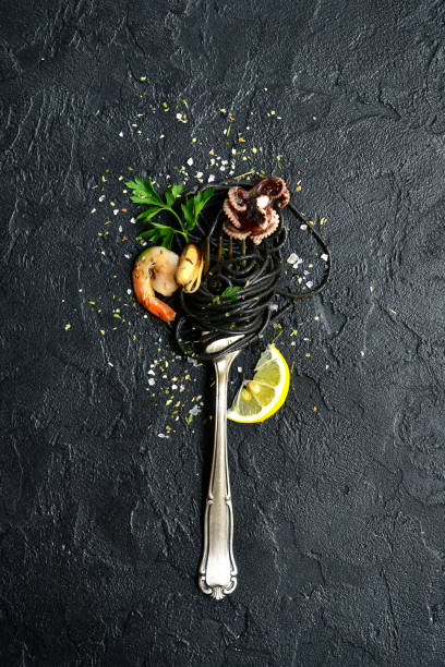 Black seafood spaghetti on fork Black seafood spaghetti on fork over black slate, stone or concrete background.Top view with copy space. food styling stock pictures, royalty-free photos & images