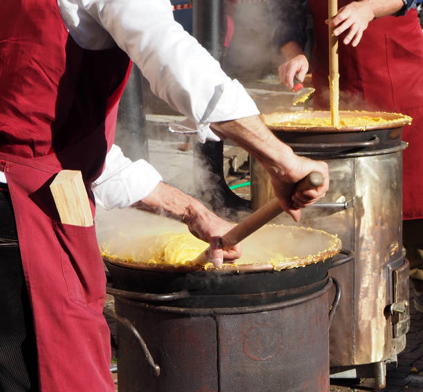 dois cozinheiros cozinhar a polenta a maneira tradicional de leste norte da itália em pequenos fogões de lenha - polenta cooking food spoon - fotografias e filmes do acervo