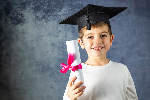 Portrait of young boy with a graduation cap and a diploma