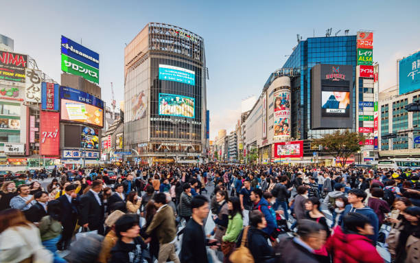 Busy Crowded Tokyo Shibuya Crossing Japan People crossing the crowded famous Shibuya Crossing in Downtown Tokyo, illuminated Shibuya Buildings with billboards in the background. Twilight light, close to sunset. Shibuya Crossing, Shibuya Ward, Tokyo, Japan, Asia. tokyo crowds on the famous shibuya crossing japan stock pictures, royalty-free photos & images
