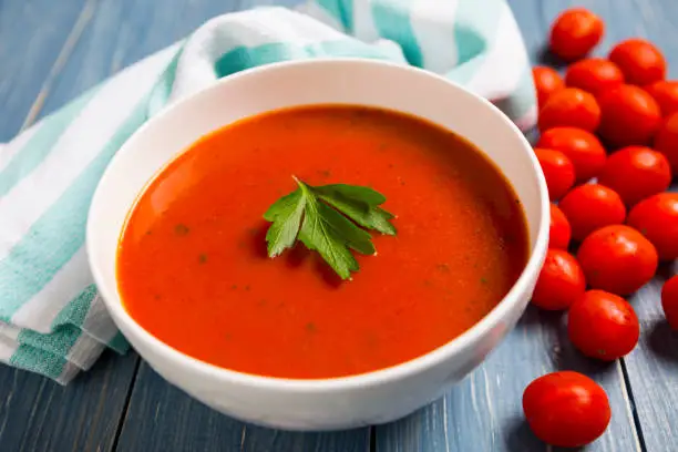 Bowl of tomato soup on blue surface with fresh tomatoes