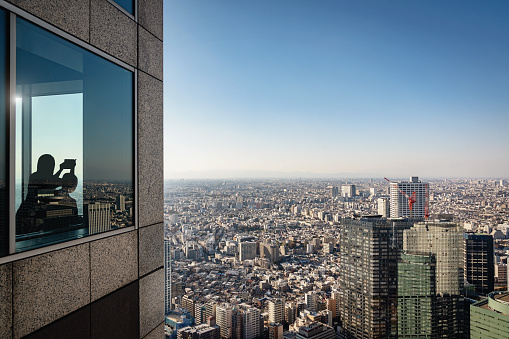 Silhouette of a unrecognizable person overlooking Tokyo Cityscape on a sunny autumn day. Taking pictures with mobile phone together. Shinjuku, Tokyo, Honshu, Japan, Asia.