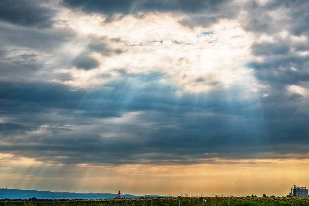 vista da estrada para kovilj a cidade e a montanha de fruska gora da sérvia. nuvens negras sobre a cidade urbana com raios de sol penetrando pela. - penetrating - fotografias e filmes do acervo