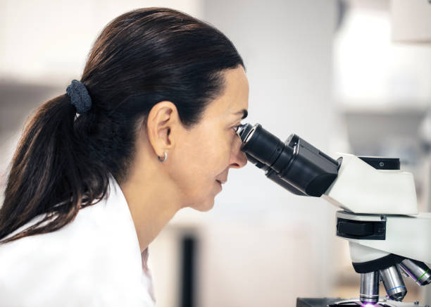 istock Female scientist looking through a microscope in a clinical laboratory isolated on white, close up 1079264364