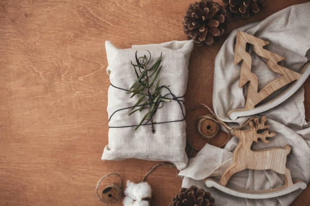 istock Simple eco presents plastic free. Zero waste  holidays. Stylish christmas rustic gift wrapped in linen fabric with green branch on wooden table with pine cones, tree,reindeer, twine, cotton. Flat lay. 1079265450