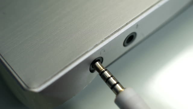 Male hand plugging headphone jack into laptop, analog signals, computer audio