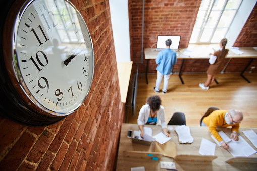 Face of clock hanging on brick wall of modern office where group of casual employees working
