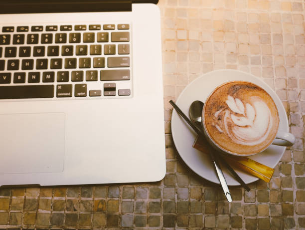 A cup of cappuccino coffee or chocolate cacao in a white cup with laptop on table