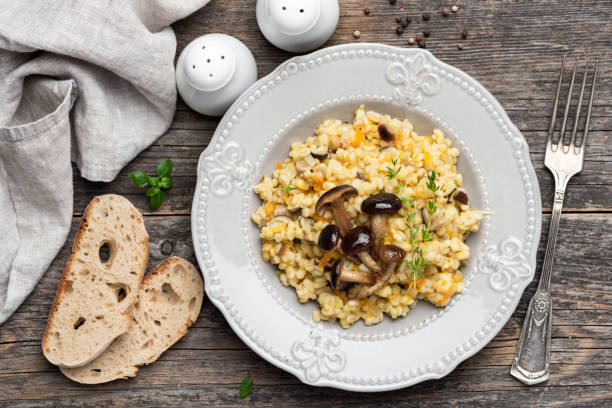 A vegan risotto with roasted pumpkin, mushrooms, and fresh spinach served in a white bowl on a light background, top view