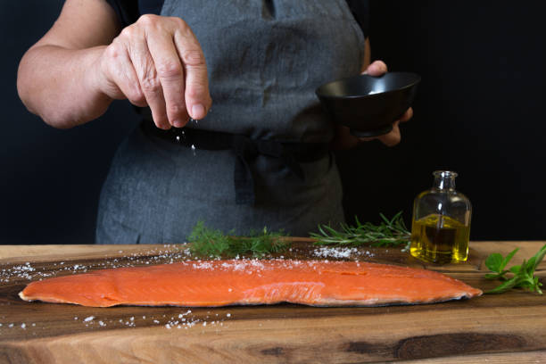 femme en ajoutant du sel sur le saumon - prepared fish photos et images de collection