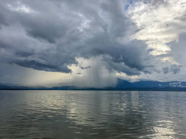 Photo of Dark clouds with rainy in storm day on the lake and mountain background. Raindrop only some area. Soft focus of clouds.