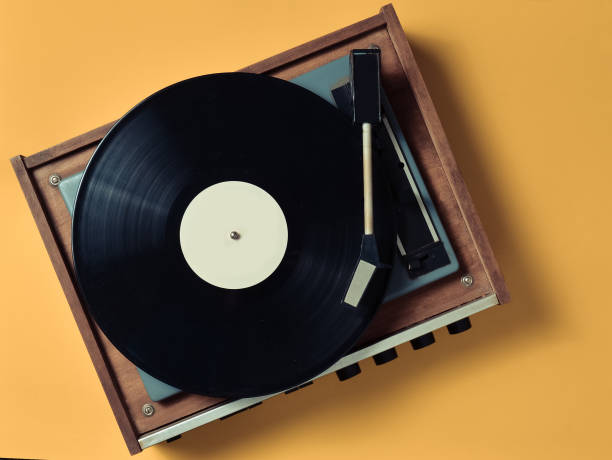 Vintage vinyl turntable with vinyl plate on a yellow pastel background. Entertainment 70s. Listen to music. Top view. stock photo