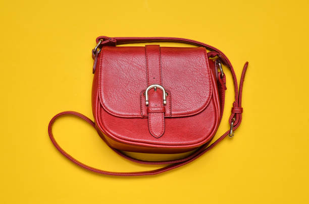 istock Red leather bag on a long strap on a yellow background. Women's accessories. Top view. 1079471698