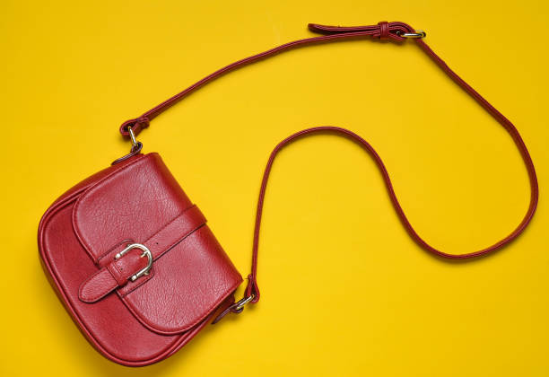 istock Red leather bag on a long strap on a yellow background. Women's accessories. Top view. 1079471736