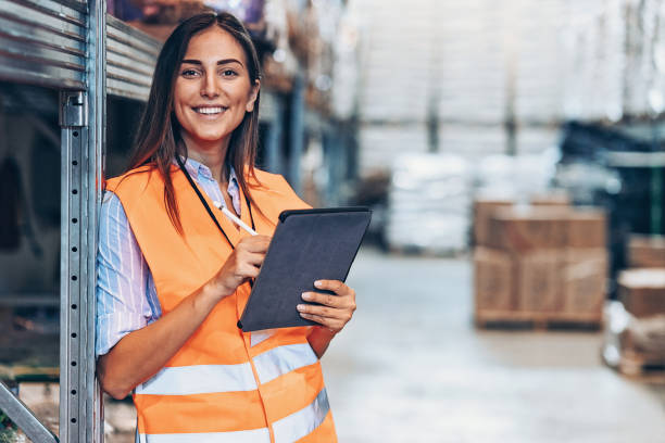 Warehouse manager with digital tablet Smiling young woman with digital tablet in a large warehouse waistcoat stock pictures, royalty-free photos & images