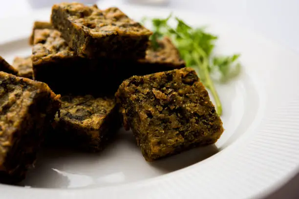 Photo of A savory cilantro cake or kothimbir vadi in square shape which is first steamed and then fried until crisp. popular indian snack served with hot tea and tomato ketchup
