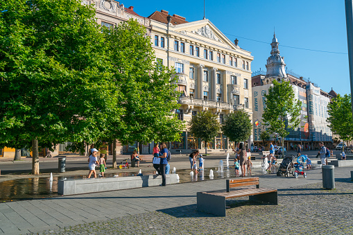 Cluj-Napoca, Romania - July 12, 2016: Cluj-Napoca  view showing Burbling fountain in Unirii square, buildings, church, trees and people playing in the fountain and walking on the street can be seen on the background