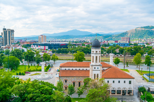 Skopje, Republic of Macedonia - July 19, 2016: view showing Skopje City with the view of Holy Mother of God Church and its bell tower, buildings, houses, fountain, river, street cars, trees and mountains can be seen on the background